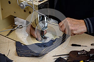 Hands of repairman fixing problems with professional industrial sewing machine in shoemaker workshop. Testing of machine
