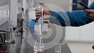 Hands of a research scientist pouring a colourless chemical using a micropipette from a conical flask to a beaker