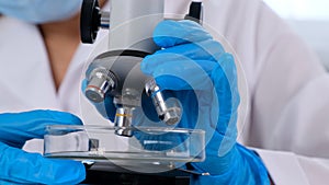 Hands of a researcher laboratory assistant in protective gloves holding a microscope in the laboratory, close up.