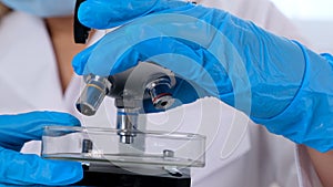 Hands of a researcher laboratory assistant in protective gloves holding a microscope in the laboratory, close up.