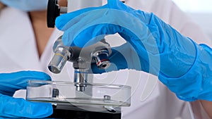 Hands of a researcher laboratory assistant in protective gloves holding a microscope in the laboratory, close up.