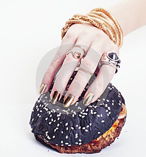 Hands of rich woman with golden manicure and jewelry holding black hamburger closeup fashion concept