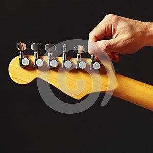 Hands of rock guitarist tunes the electric guitar on black background