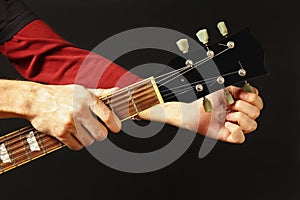 Hands of rock guitarist tunes the guitar on dark background