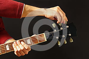 Hands of rock musician tunes the guitar on dark background