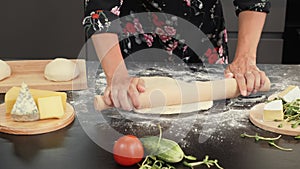 Hands roll out dough with rolling pin on wooden table. Female preparing fresh dough with rolling pin on kitchen table. Woman cooki