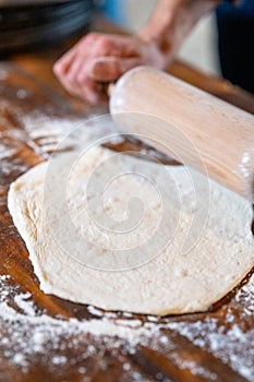 Hands rolling out dough on floured wooden background