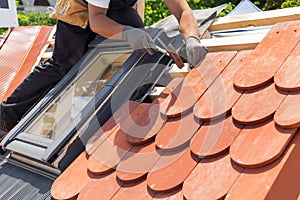 Hands of roofer laying tile on the roof. Installing natural red tile using hammer.