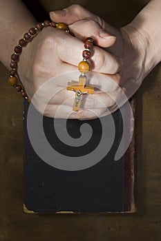 Hands with rosary and an old book