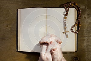 Hands with rosary and an old book