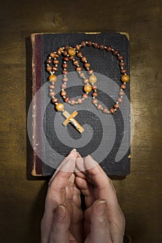 Hands with rosary and an old book