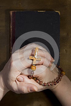 Hands with rosary and an old book