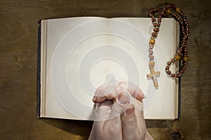 Hands with rosary and an old book