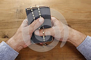 Hands with rosary over old Holy Bible