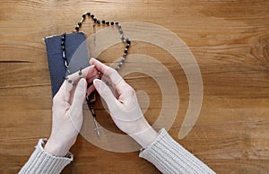 Hands with rosary over old Holy Bible