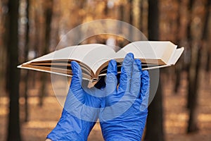 Hands in rubber gloves hold book in forest