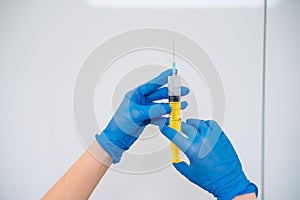 Hands in rubber gloves hold a disposable medical syringe with the drug