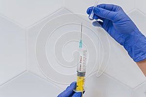 Hands in rubber gloves hold a disposable medical syringe with the drug