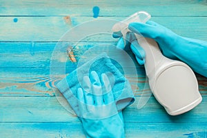 Hands in rubber gloves holding blue microfiber cleaning cloth and cleaning bottle with spraying liquid