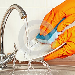 Hands in rubber gloves wash the dirty dishes under running water in kitchen