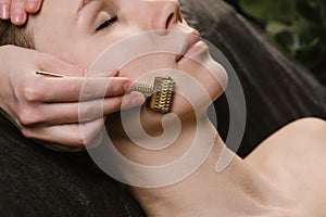 Hands rubbing gua sha spiked roller on a woman`s face at asian beauty clinic