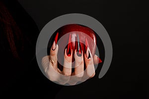 Hands with scary nails manicure holding poisoned red apple