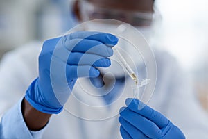 Hands, scientist and dropper in test tube for research, chemical liquid and vaccine in container. Gloves, doctor and