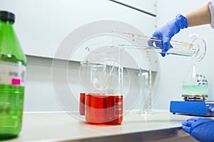 Hands of the scientist in the laboratory mixes with transfusion a chemical materials from graduated cylinder to beaker. Concept