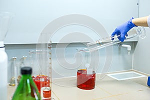 Hands of the scientist in the laboratory mixes with transfusion a chemical materials from graduated cylinder to beaker. Concept