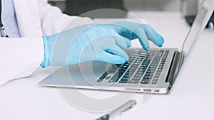 Hands of a scientist in surgical gloves, typing on a laptop in a medical lab. Closeup of a healthcare professional