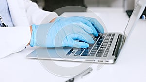 Hands of a scientist in surgical gloves, typing on a laptop in a medical lab. Closeup of a healthcare professional
