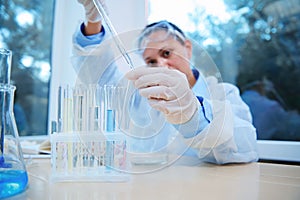 The hands of a scientist using a graduated pipette, titrate the reagent into test tubes during a scientific experiment