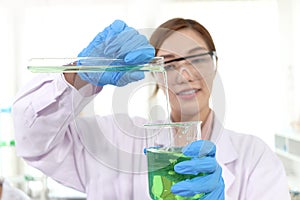 Hands of scientist woman in lab coats with safety glasses pouring chemical from test tube into beaker to do science experiment.