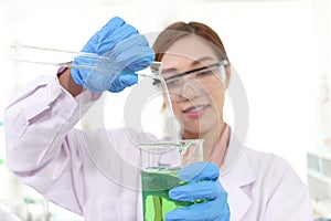 Hands of scientist woman in lab coats with safety glasses pouring chemical from test tube into beaker to do science experiment.