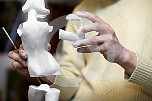 Hands of sculptor hold parts of statuette. photo