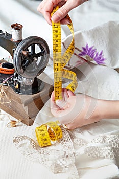 Hands of seamstress hold sewing centimeter. Next to sewing machine