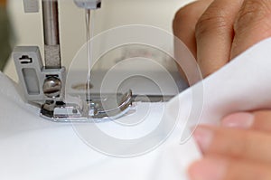 Hands seamstresses with white material behind the sewing machine.