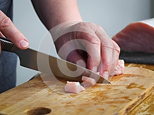 Hands of a seigners woman cutting a raw pork meat fillet on a wooden board with a knife