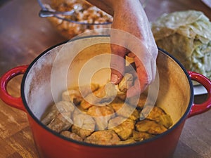 Hands of a seigners woman laying raw sauerkraut stuffed cabbage and rice-meat stuffing in a cast-iron pan