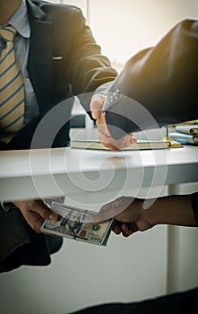Hands sending money under corrupt bribery Close-up of two businessmen shaking hands and taking bribes under a wooden table in the