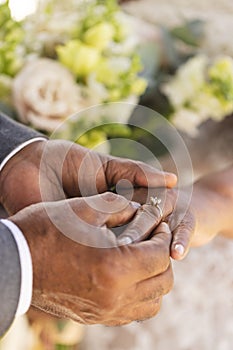 Hands of senior biracial groom putting wedding ring on finger of his bride