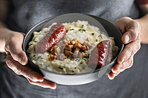 The hands of a senior home cook hold a plate with a national Slovak dish - Bryndzove Halusky