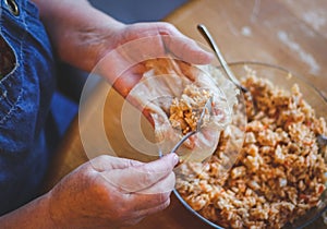 The hands of a senior woman hold a raw leaf of sauerkraut and put a metal teaspoon of rice-meat