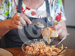 The hands of a senior woman hold a straightened leaf of sauerkraut in the palm and put a rice-meat