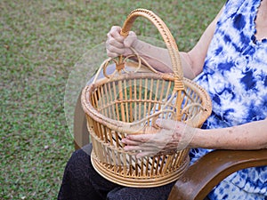 Hands of a senior woman holding a basket while sitting on a chair in a garden. Space for text. Concept of aged people and