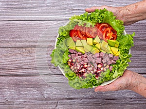 Hands of a senior woman holding a dish green lettuce salad.