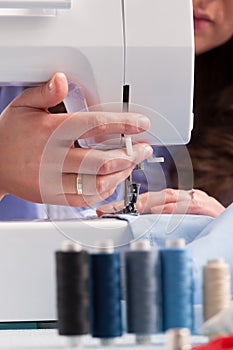 Hands on sewing machine with reels of colour threads and sewing