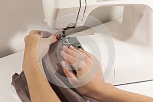 Hands sewing on white machine brown fabric