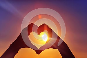 Hands in the shape of a heart against sunlight in the sunset sky, dusk. Symbol of love