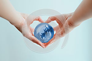 Hands in shape of heart  holding blue glass globe of indoneasia and Phillipine sea
